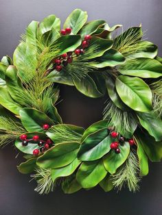 a green wreath with red berries and greenery on the front door is ready to be hung