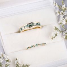 two wedding rings sitting on top of a white box next to some flowers and greenery