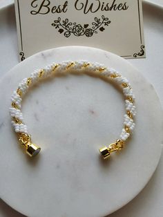 a white beaded bracelet with gold bells on it and a card for best wishes