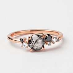 three stone ring in rose gold with black and white diamonds on the band, set against a plain background