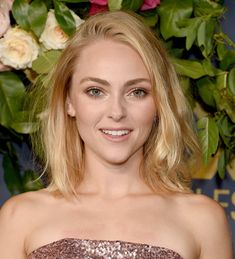 a woman with blonde hair wearing a strapless dress and smiling at the camera while standing in front of flowers