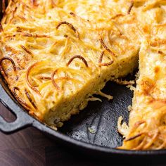 a skillet with some food in it on a wooden table and one slice missing