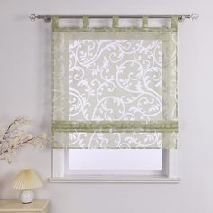 a white and green roman blind in a living room with a lamp on the side table