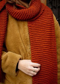 a woman wearing an orange knitted scarf with a ring on her left hand, standing in front of a wooden door