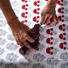 two hands are holding something on top of a table with red and white floral designs