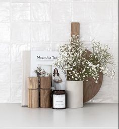 a vase with flowers and candles next to a book on a shelf in front of a white tiled wall