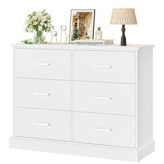 a white dresser with drawers and a lamp