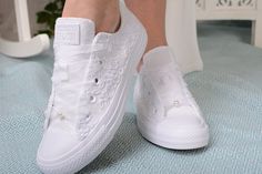 a woman's feet wearing white shoes with lace and pearls on the side, sitting on a bed