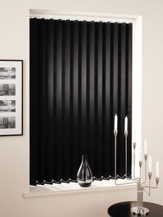 black vertical blinds in the corner of a room with candles and pictures on the wall