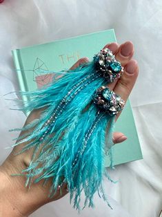 a woman's hand holding two hair clips in front of a book with beads and feathers on it