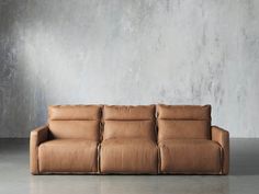 a brown leather couch sitting in front of a wall with concrete walls and cement flooring