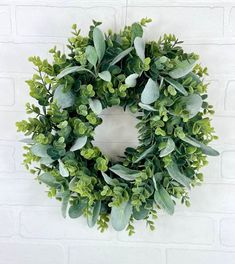 a wreath with green leaves hanging on a brick wall