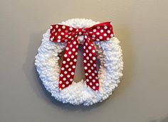 a white wreath with red and white polka dot ribbon hanging on the wall next to a gray wall