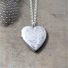 This sterling silver locket is beautifully engraved with a floral swirling plume design on the front; the reverse has been engraved from the previous owner "Elaine 1973 Love, Mom and Dad".  The heart shaped locket opens revealing two compartments awaiting your treasured photos.  The pendant is suspended from a  new sterling silver chain accented with tiny ruby rondelles (July birthstone) at the lobster clasp closure.Locket 30x22mmNecklace 24" (61cm)✤Our entire selection of lockets can be found h Antique Silver Heart Locket Jewelry, Victorian Silver Heart Pendant Locket Necklace, Antique Silver Engraved Locket Necklace For Anniversary, Silver Heart-shaped Etched Necklace, Heirloom Silver Heart Pendant Jewelry, Antique Silver Engraved Heart Jewelry, Engraved Antique Silver Locket Necklace For Anniversary, Etched Heart Silver Necklace, Heart Pendant Jewelry With Engraving Option For Weddings