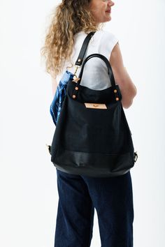 A woman wearing the black backpack with black straps and the meanwhile logo and a blue decorative scarf. Rooster Logo, Wax Canvas, Lynchburg Virginia, Black Convertible, Waxed Canvas Backpack, Hard Working Women, Waxed Canvas Bag, English Bridle, Top Straps