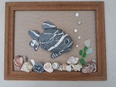 there is a fish made out of rocks and sea shells in a frame on the wall