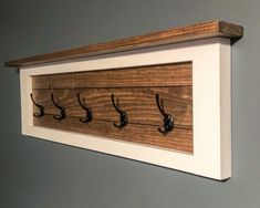 a wooden coat rack with five hooks on it and two coats hanging from the wall