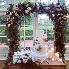 a wedding cake and cupcakes on a table in front of an open window