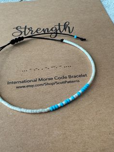 "Strength" Morse Code Bracelet.  ⭐️ Materials - Bracelet made on black, waxed-cotton cord that is durable and lightweight. The morse code message is made with glass seed beads: message colors are white dashes and ocean blue dots.  Bracelet is adjustable with a sliding macrame knot- bracelet fits most wrist sizes.  Bracelet comes packaged on card-stock for your Morse Code Message as shown.  Message me if you have any questions. Bracelet Materials, Morse Code Bracelet, Bracelet Minimalist, Blue Dots, Macrame Knot, Bracelet Dainty, Dainty Bracelet, Knot Bracelet, Motivational Gifts