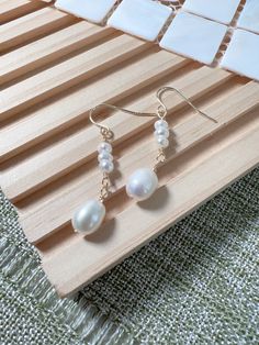 Grace your ears with the enchanting allure of these handcrafted freshwater pearl drop earrings. Each earring features a delicate cascade of petite pearls leading to a singular, lustrous pearl drop, glowing with soft, natural tones. The warm gold-tone hooks complement the pearls' ethereal beauty, creating a harmonious balance between rustic charm and refined elegance. These earrings are not just an accessory, but a statement of sophistication, perfect for bringing a touch of class to both casual Graceful Pearl Dangle Earrings, Graceful Pearl Earrings With Pearl Charm, Graceful Pearl White Pearl Earrings, Akoya Pearl Drop Dangle Earrings, Akoya Pearl Drop Earrings, Graceful Pearl White Dangle Pearl Earrings, Minimalist Akoya Pearl Drop Earrings, Handmade Delicate Pearl Earrings, Akoya Pearl Drop Teardrop Earrings