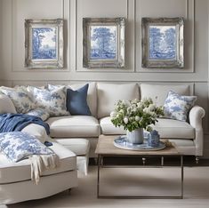 a living room with white furniture and blue pillows on the couches in front of two framed pictures