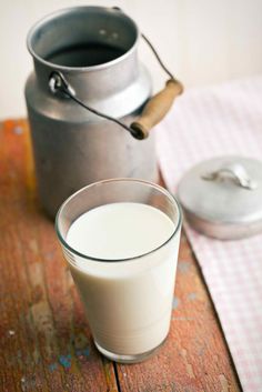 a glass of milk sitting on top of a wooden table next to a metal pot