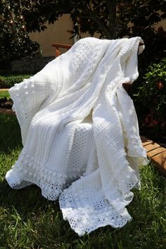 a white crocheted blanket sitting on top of a grass covered ground next to a wooden bench