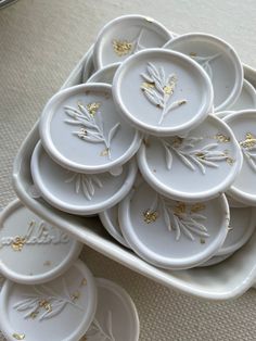 white dishes with gold leaf designs are stacked on top of each other in a tray