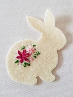 a white felt bunny with pink flowers on it's back and green leaves around its ears