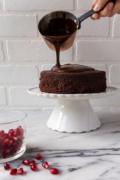 someone pouring chocolate sauce on top of a cake with pomegranates around it