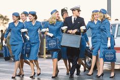 a group of women in blue uniforms walking down the street with suitcases on their backs