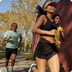 two people running in the street near a brick wall