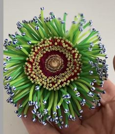 a hand holding a flower made out of green and red beads on it's center