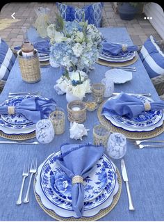 a table set with blue and white plates, napkins, silverware and flowers