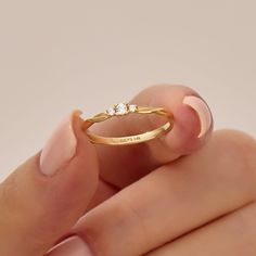 a woman's hand holding a gold ring with two diamonds on it and the middle finger