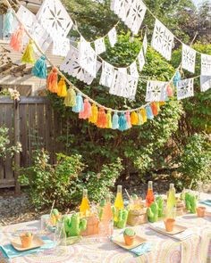 an outdoor party with colorful paper decorations and drinks on the table, in front of a wooden fence