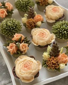 cupcakes decorated with flowers and succulents are on a white tray