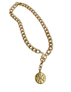 This snake chain necklace commands attention with its bold design and luxurious appeal. Crafted from gleaming gold, each link in the chain is substantial, exuding a sense of opulence and strength. At its center lies the focal point of the piece: a large gold charm shaped like a compass rose, with distinct north, south, east, and west directions. The charm is intricately detailed, its smooth surface catching the light and casting a warm, radiant glow. Completing the necklace is a gold toggle clasp, adding both functionality and style to the piece. The total length is 20 inches with the clasp right at 18 inches. When worn, this statement necklace becomes more than just an accessory; it becomes a symbol of confidence, sophistication, and timeless elegance. Its weight on the neckline serves as Gold-plated Round Pendant Charm Necklaces, Gold-plated Charm Necklaces With Round Pendant, Gold Plated Charm Necklaces With Round Pendant, Gold Plated Charm Necklace With Round Pendant, Brass Pendant Necklace With Gold Chain, Luxury Gold Charm Necklace With Adjustable Chain, Luxury Gold Charm Necklaces With Adjustable Chain, Gold-plated Necklace With Round Pendant, Gold-tone Pendant Medallion Necklace