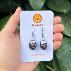 a pair of black and red smiley face earrings on a card with green leaves in the background