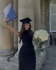 a woman in a graduation gown holding a bouquet of flowers and a diploma cap on her head