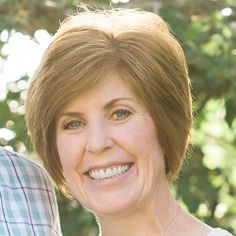 a close up of a person wearing a necklace and smiling at the camera with trees in the background