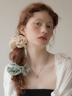 a woman with red hair wearing a white shirt and green flower in her hair is looking at the camera