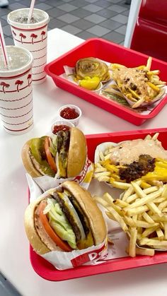 two trays filled with sandwiches and fries on top of a table next to drinks