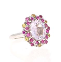 This beautiful ring has a Oval Cut 3.81 carat Kunzite that is set in the center of the ring and is surrounded by 24 Round Cut Pink and Yellow Sapphires that weigh 1.13 carats. The total carat weight of the ring is 4.94 carats. The Kunzite measures at 9 mm x 11 mm. The ring is made in 14K White Gold and weighs approximately 6.6 grams. Complimentary ring sizing is available upon request. Oval White Sapphire Ring, Oval White Sapphire Ring With Center Stone, Oval White Sapphire Ring With Halo Setting, Dazzling Oval Multi-stone Cluster Ring, White Oval Sapphire Gemstone Ring, White Oval Sapphire Ring With Center Stone, Luxury White Sapphire Oval Ring, Pink Round Amethyst Ring Fine Jewelry, Exquisite Pink Sapphire Round Rings