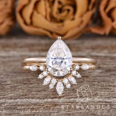 an engagement ring with a pear shaped diamond surrounded by small white and clear stones, on top of a wooden surface