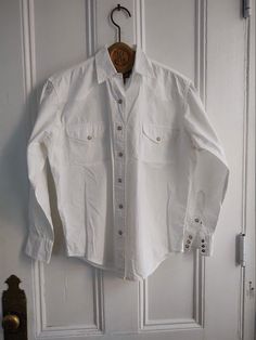 "Classic western ranch style Calvin Klein shirt with pearl snaps down the front, three on each cuff.  Solid white shirt with slightly tailored fit. In very good condition. No holes.  MEASUREMENTS Chest 44\" Sleeve 22.5\" 100 % cotton Machine wash. Easy to care for. PLEASE READ: Our products are vintage and some are handmade. Some are new and unused but can still have signs of age from storage. If you are particular or a perfectionist please do not order. It is assumed you have read the shop policies before ordering." Classic Shirt With Pockets For Rodeo, Classic Button-up Top For Rodeo, Western Style Button-up Ranch Shirt, Western Style Button-up Shirt For Ranch, Classic Collared Top For Rodeo, Casual Shirt With Button Closure For Western-themed Events, White Western Tops For Country Events, White Fitted Top For Western-themed Events, Western Style Button-up Shirt For Western-themed Events