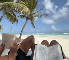 a man reading a book while sitting on a beach chair under a palm tree with the ocean in the background