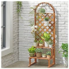 a bamboo plant stand with potted plants on it in front of a brick wall