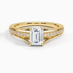 a yellow gold ring with an emerald stone and diamonds on the band, set in 18k