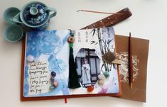 an open book with pictures and writing on it sitting next to a teapot, pen and spoon